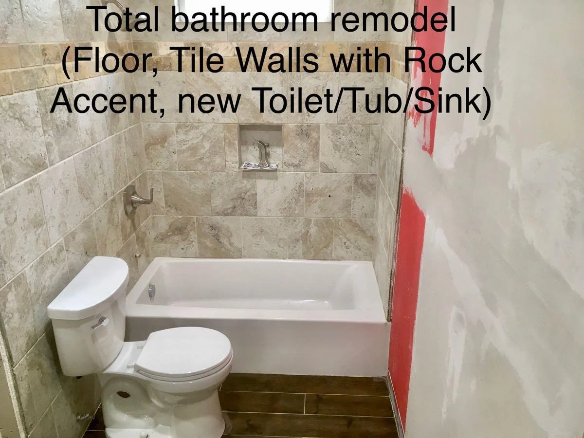 Bathroom remodel with a tiled tub surround, rock accent, sink and toilet